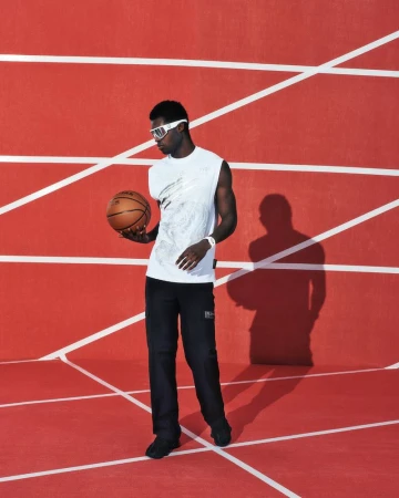 Athletic Black man with basketball on red indoor track. Man in sports goggles, white shirt, and black pants poses with ball in hand.