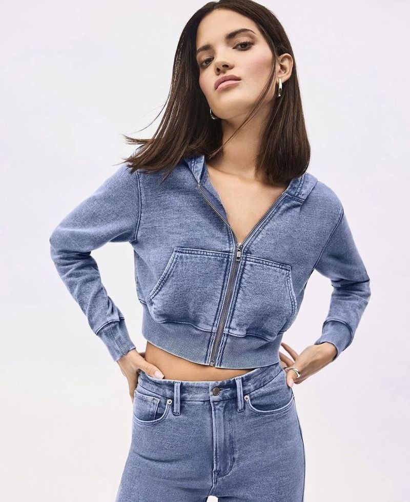 Woman in a cropped denim jacket and jeans poses in a studio setting, looking stylish in this fashion-forward shot.