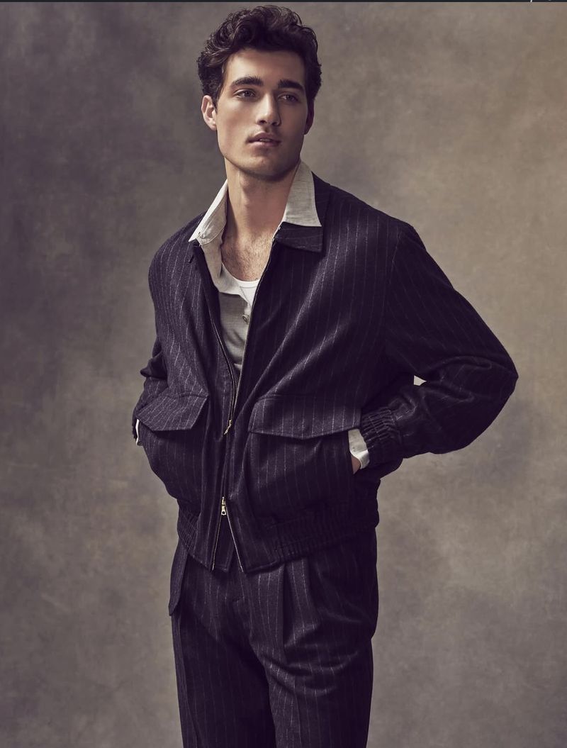 Portrait of a young adult male in a pinstripe suit jacket and pants, with a white collared shirt, posing in a studio setting.