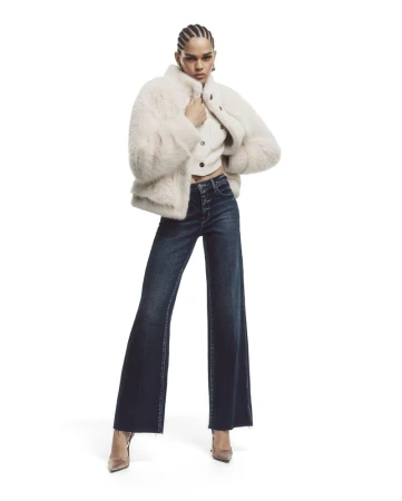 Hiandra Martinez posing in an off-white plush jacket and dark wide-leg denim jeans against a white seamless studio background.