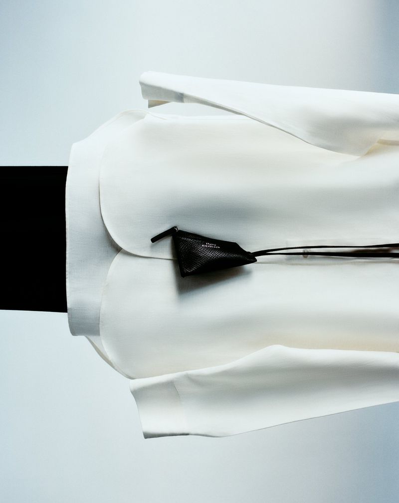 Close-up studio shot of a modern white jacket paired with a small black leather pouch, against a contrasting black and white backdrop.