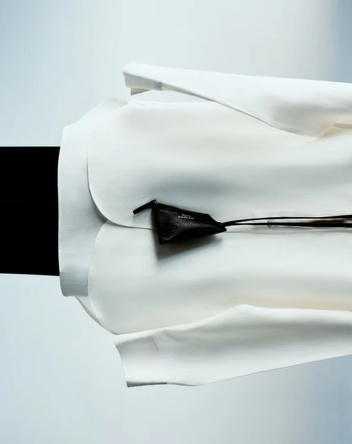 Close-up studio shot of a modern white jacket paired with a small black leather pouch, against a contrasting black and white backdrop.
