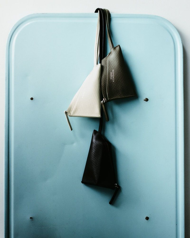 Three pyramidal purses are hanging from a hook against a light blue background. The purses are varying shades of black and white.