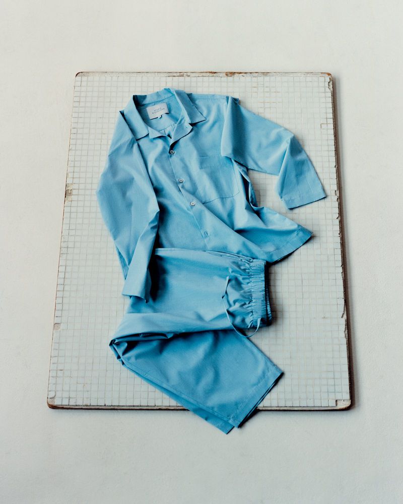 Light blue pyjama set laid flat on a vintage tiled surface, featuring a button-down shirt and drawstring trousers, styled indoors.