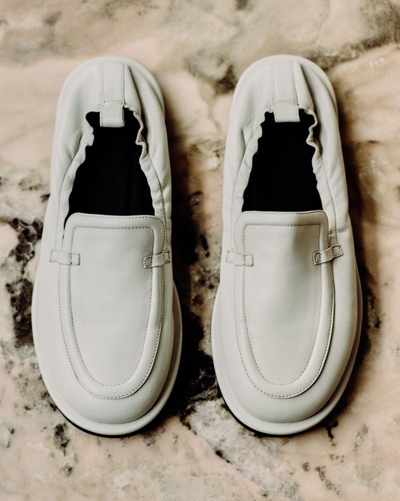 Overhead shot of light grey leather slip-on shoes on a marble surface showcasing minimalist design, clean lines, and neutral color palette.