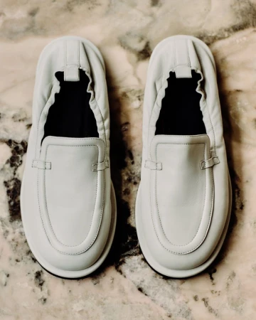 Overhead shot of light grey leather slip-on shoes on a marble surface showcasing minimalist design, clean lines, and neutral color palette.