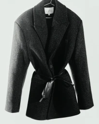 Studio Nicholson black blazer jacket hanging on a wire hanger against a neutral white background