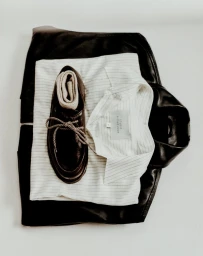 Top-down flat lay featuring a black leather jacket, striped button-down shirt, and dark leather shoe with a ribbed sock inside.