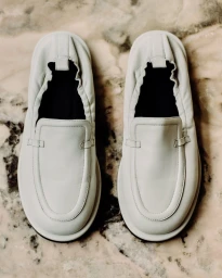 Pair of off-white leather slip-on loafers placed flat on a neutral veined marble surface.