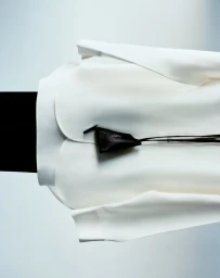 Close-up product shot of a white structured garment with a small black triangular pouch attached by strings.