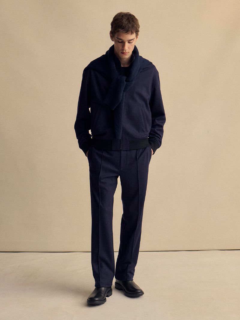 Male fashion model in navy jacket, scarf, and trousers against neutral backdrop. Classic style for apparel and online product catalog.