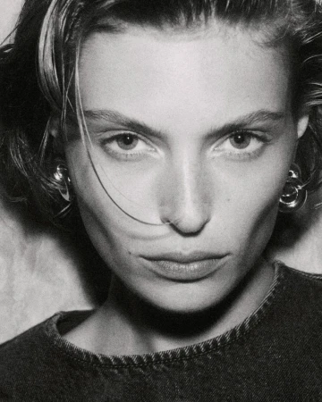 Close-up monochrome portrait of a female model wearing silver earrings and a dark denim top.