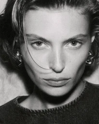 Close-up monochrome portrait of a female model wearing silver earrings and a dark denim top.