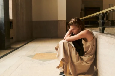 Model seated on stone floor wearing beige dress in interior hallway for COS Fall Womenswear 24