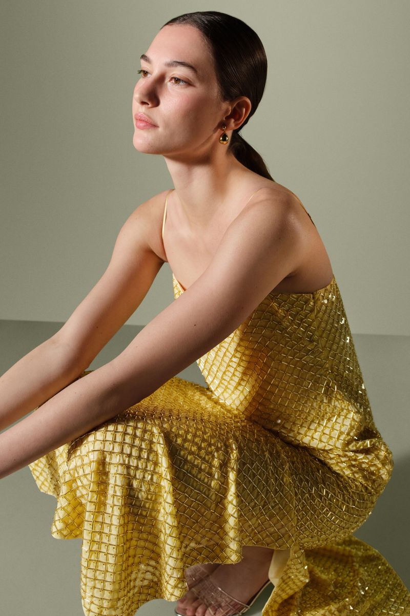 Adult woman in golden sequin gown posing in studio with neutral background and soft lighting for fashion editorial photography.