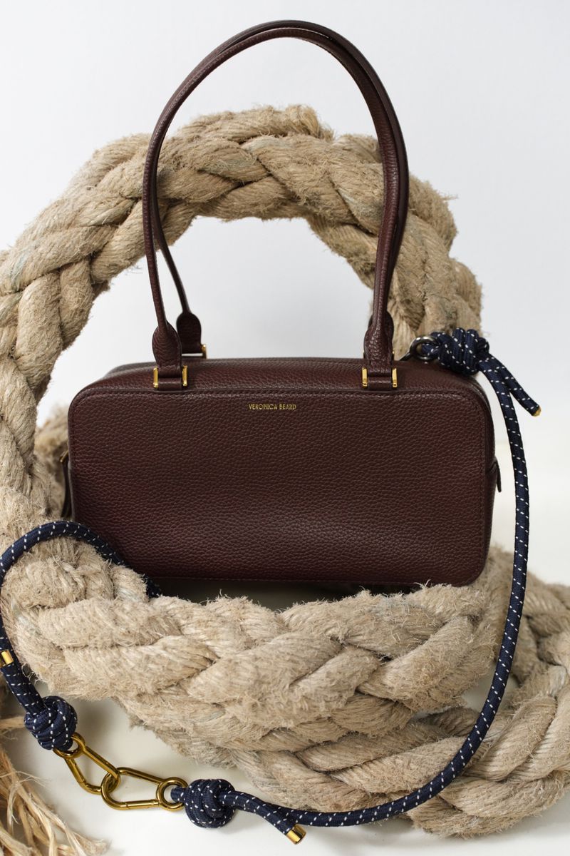 Close-up of a dark brown leather bag with double handles, accented with a braided rope and blue and white rope strap.