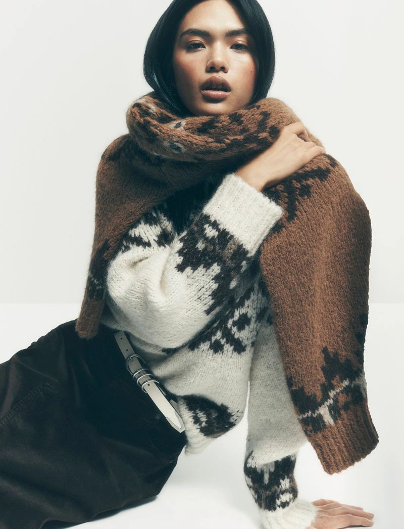 Model wearing a patterned knit sweater and brown scarf against a plain white studio background for Bloomingdale's.