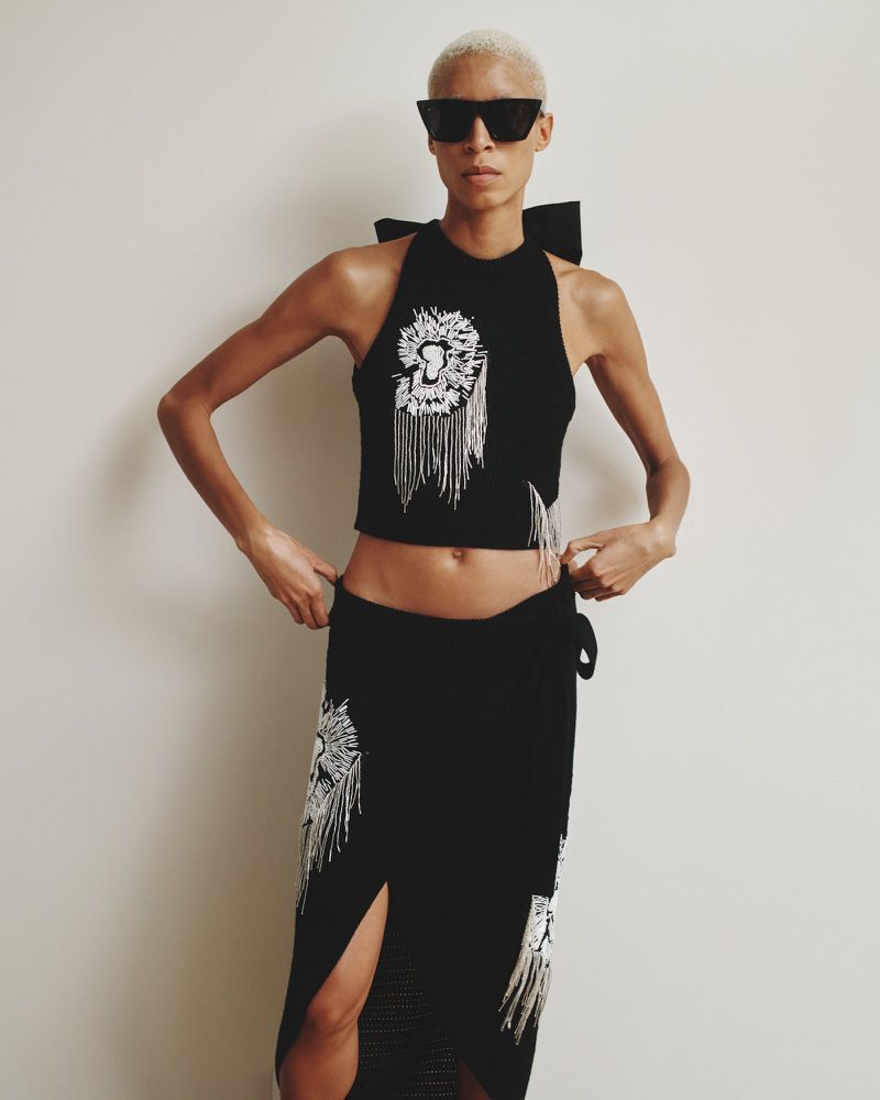 Woman in black halter top and maxi skirt with white lion graphics poses indoors wearing sunglasses in a fashion editorial style.