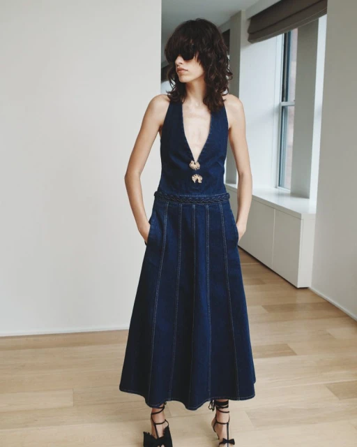 Fashion model in a blue denim dress, posing in a studio with natural light, showcasing a modern and stylish design with unique details.
