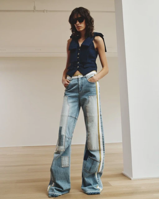 Woman in a navy vest and wide-leg patchwork jeans posing in a studio setting with a neutral background and natural lighting.