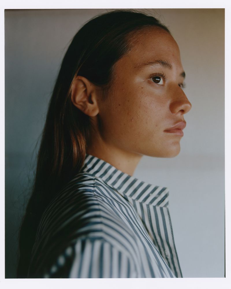 Portrait of a woman with long brown hair wearing a striped shirt, captured in a close-up studio shot with neutral background.