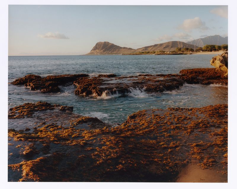 Scenic ocean view with rocky shoreline and waves, set against a backdrop of distant mountains under a clear sky, captured during daytime.