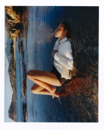 Woman wearing a white shirt and dark shorts lying on rocks by blue water