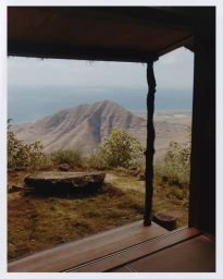 A framed view from a wooden porch looking out toward a prominent mountain and the sea in the distance.