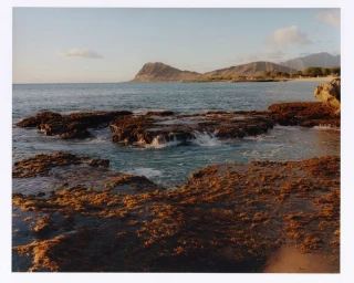 Rocky coastline and gentle ocean waves under an open sky with distant mountains for the Attersee 2025 Capsule Collection.