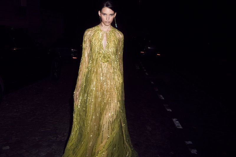 Elegant adult female model in a flowing, shimmering gold gown. The photograph is shot at night with minimal lighting and a dark background.