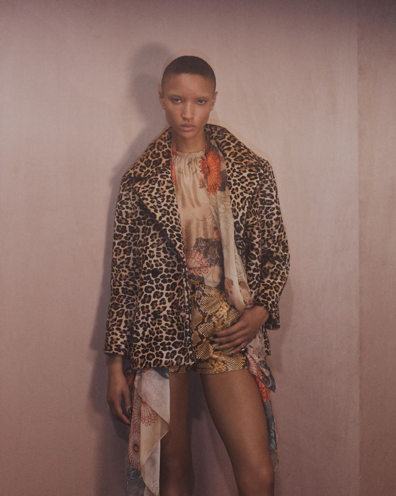 Adult woman posing in a printed coat and shorts, captured with a medium shot in an indoor setting with soft, diffused lighting.
