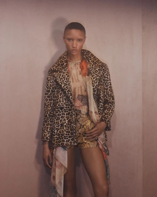 Adult woman posing in a printed coat and shorts, captured with a medium shot in an indoor setting with soft, diffused lighting.