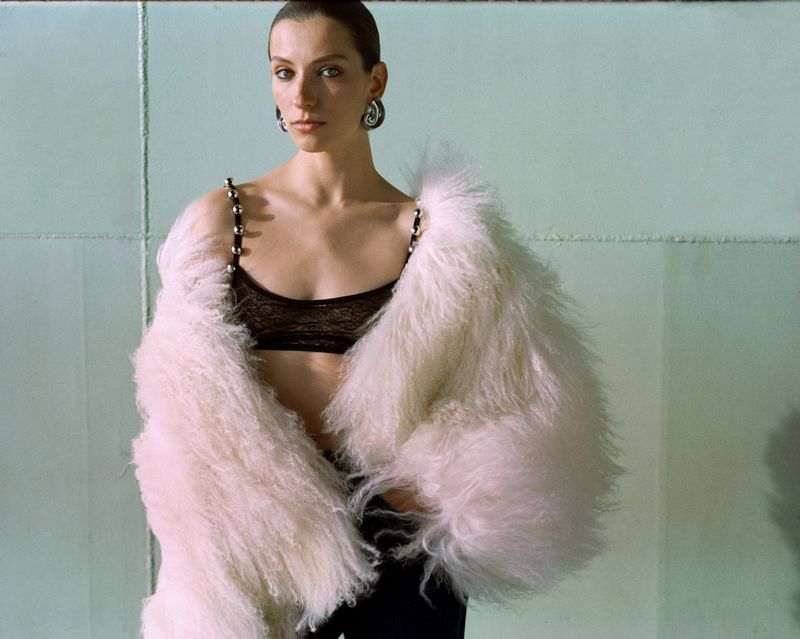 Woman in black bra and fuzzy jacket, studio shot. Fashion editorial image with cool tones, clean backdrop, and elegant styling.