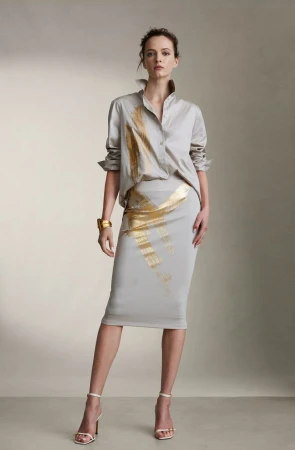 Fashion model poses in a grey satin blouse and matching pencil skirt with gold accents, paired with high heels in a studio setting.