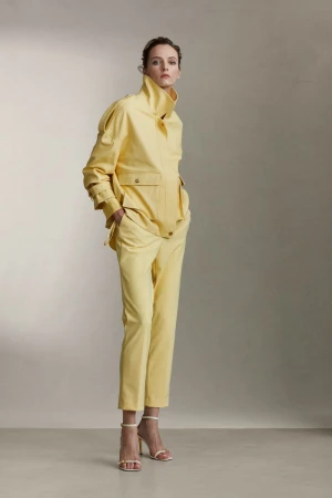 Model wearing a yellow jacket and matching trousers standing against a plain neutral studio background.