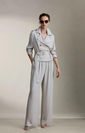 Model wearing a light grey belted jacket and trousers with sunglasses against a neutral studio backdrop