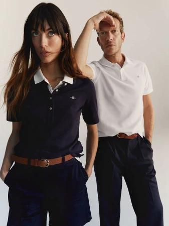 A stylish fashion shot of an adult woman and man posing in polo shirts and casual pants, shot against a neutral studio backdrop.