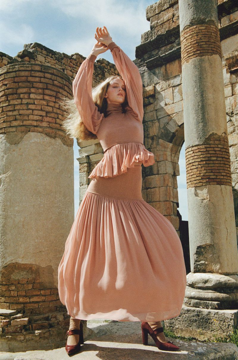 Woman posing in a long sleeve dress with column ruins in the background, creating a visually striking fashion editorial.