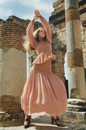 Woman posing in a long sleeve dress with column ruins in the background, creating a visually striking fashion editorial.