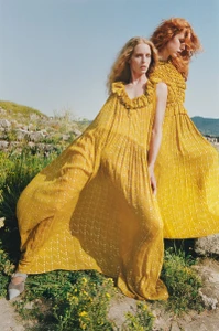 Two models wearing long yellow ruffle dresses posing outdoors on a grassy hillside under a clear sky for Ulla Johnson Autumn Winter 2024.