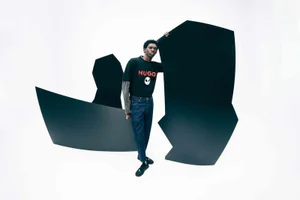 Model Ottawa Kwami posing in a graphic t-shirt and blue jeans against a white background with black geometric shapes.