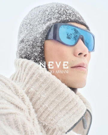 Close-up of a man wearing blue-tinted goggles and a knit cap covered in snow. He is wearing a thick knit sweater and facing right.