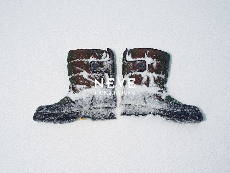 Two camouflage pattern winter boots covered in snow, set against a stark white snowy backdrop, creating a minimalist fashion statement.