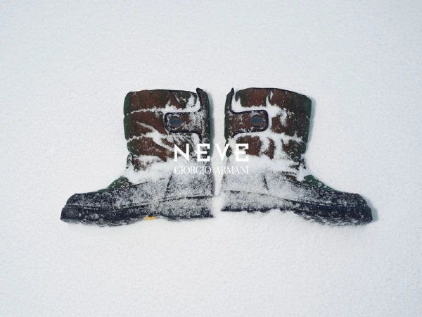 Two camouflage pattern winter boots covered in snow, set against a stark white snowy backdrop, creating a minimalist fashion statement.