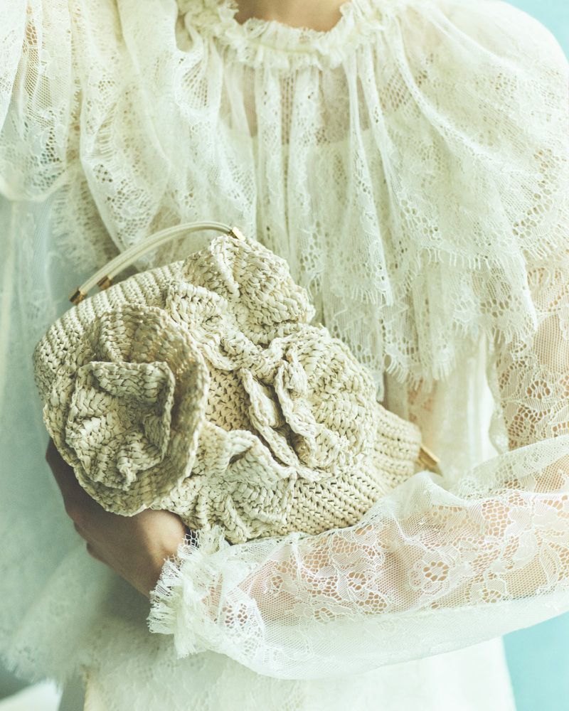 Close-up of a woman holding a decorative, textured handbag with a floral design, wearing a lace-trimmed blouse with ruffles.