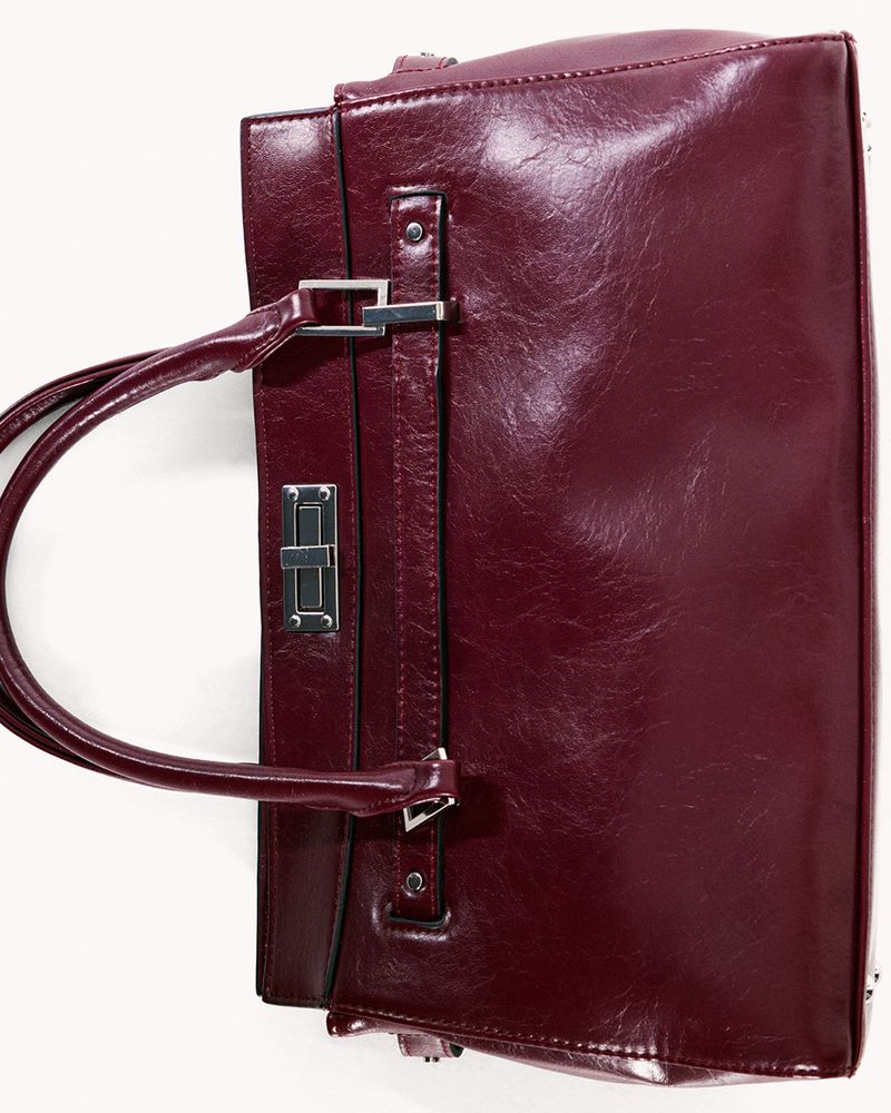Burgundy leather handbag with metal hardware on a white surface. Fashion accessory for women, isolated in a studio.