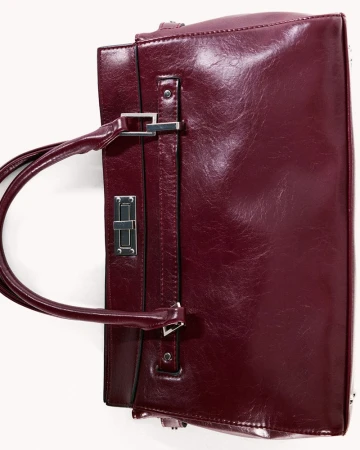 Burgundy leather handbag with metal hardware on a white surface. Fashion accessory for women, isolated in a studio.