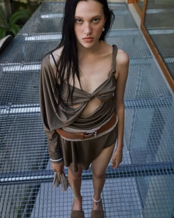 Attractive young woman poses in modern dress with brown belt and matching shoes on metal grid under skylight for a fashion shoot.