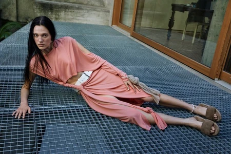 Model lying on metal grating wearing a pink draped dress with a white belt and brown sandals for ATXV lookbook