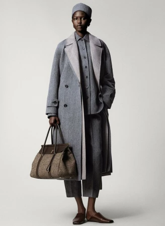 Elegant Black woman in herringbone grey wool overcoat, matching pants, shirt, and hat, carrying a brown leather bag, studio shot.